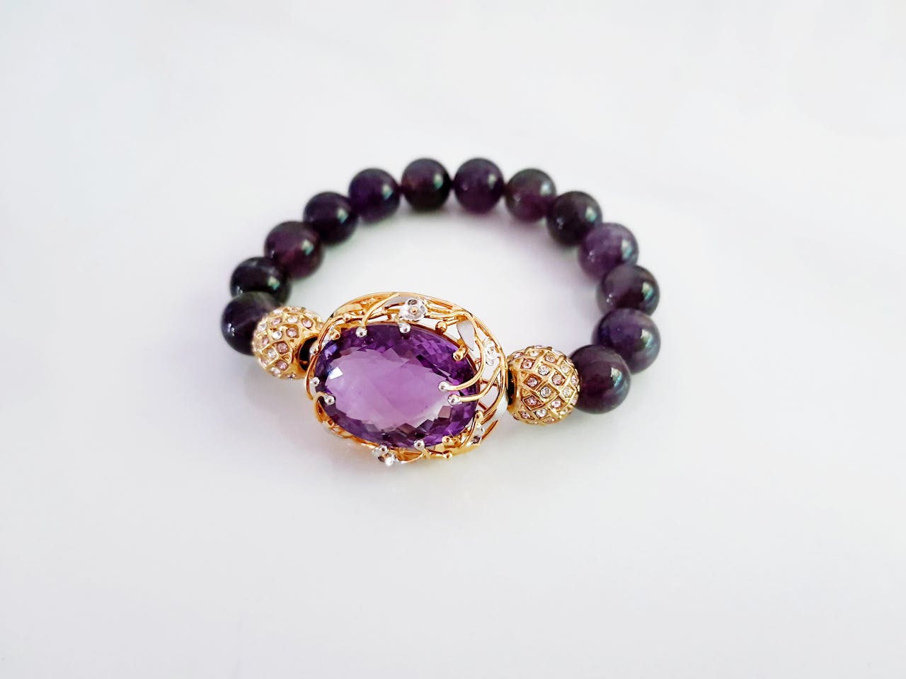 Luxurious beaded bracelet with central amethyst gemstone set in gold, on a white background.